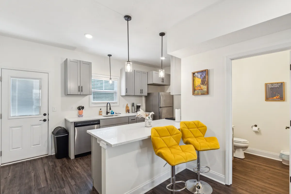 A cheerful kitchen and dining space with bold yellow bar stools set against a sleek white countertop, complemented by modern appliances. The space feels open, airy, and welcoming with stylish décor touches.