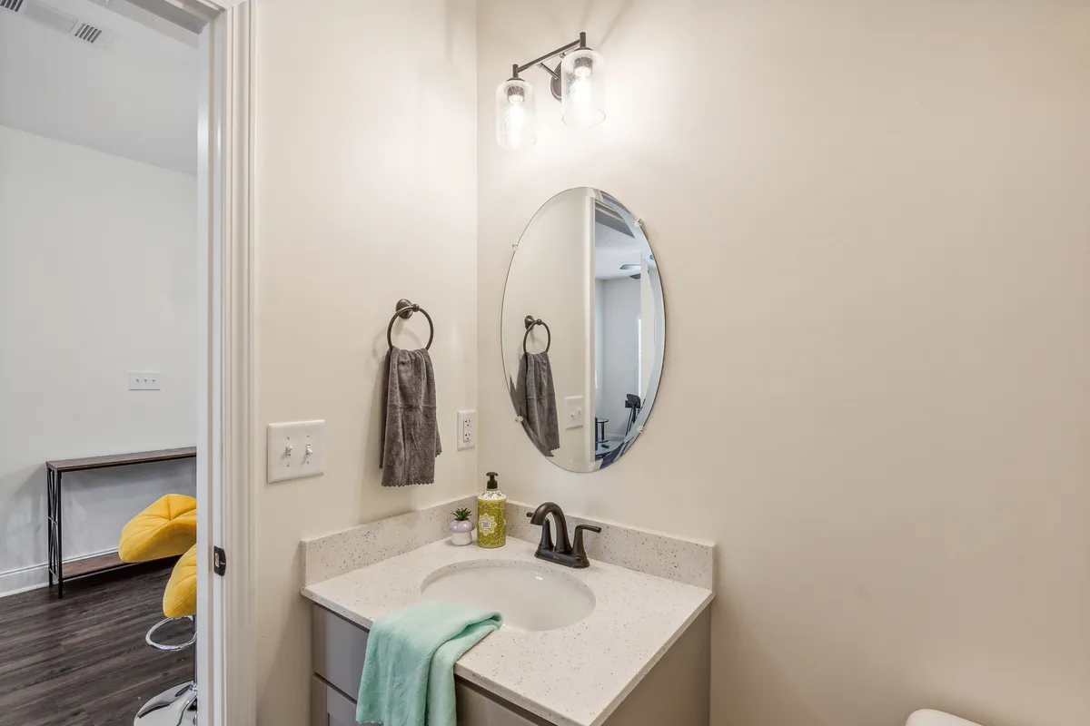 A functional yet inviting bathroom vanity with an oval mirror, modern sink, warm lighting, neatly arranged towels, and stylish accessories. The space is perfect for quick refreshes or self-care routines.