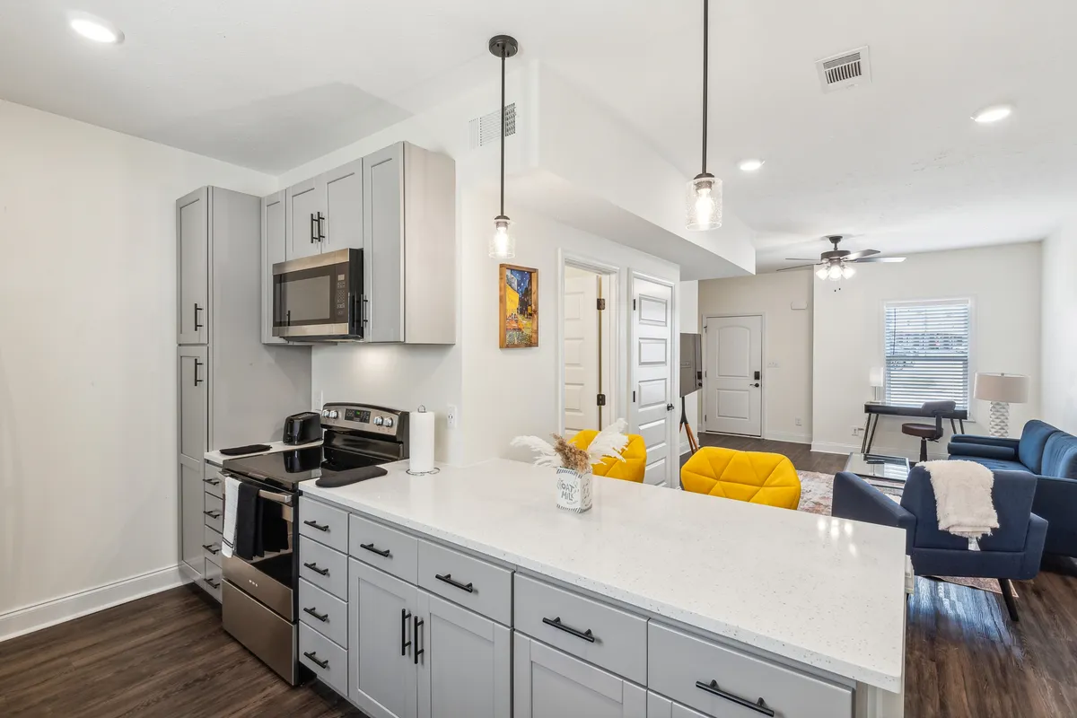 A spacious area combining a modern kitchen island with yellow accent chairs and a blue sofa situated nearby. The open layout encourages easy flow between cooking, dining, and relaxing, capturing the essence of a central hub for entertaining and togetherness.