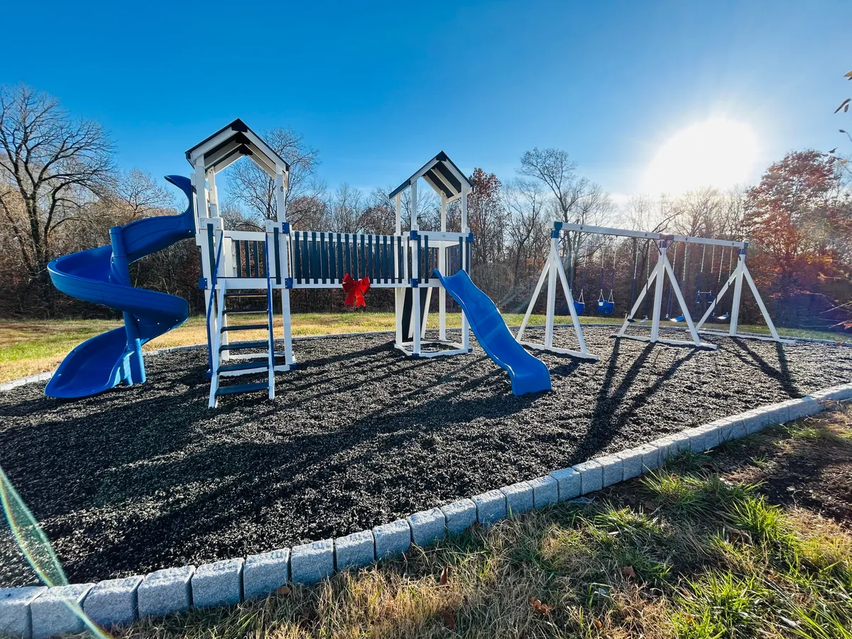 A bright, inviting playground featuring a colorful blue slide, swings, and ample space for children and families to gather. The area is surrounded by greenery, creating a lively outdoor environment perfect for recreation and relaxation.
