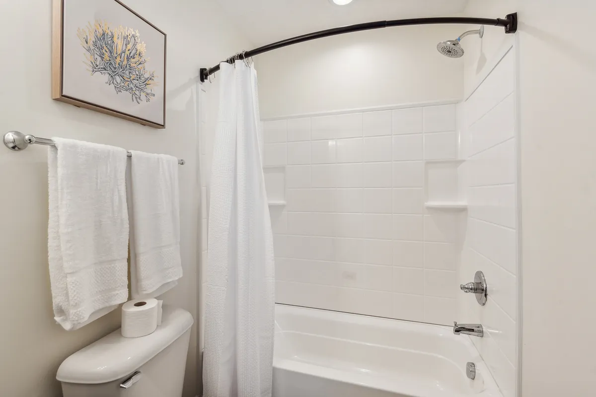 A modern bathroom featuring a deep bathtub, framed artwork on the wall, and neatly arranged towels. The space is bright and tranquil, inviting guests to unwind with a relaxing bath or refreshing shower.